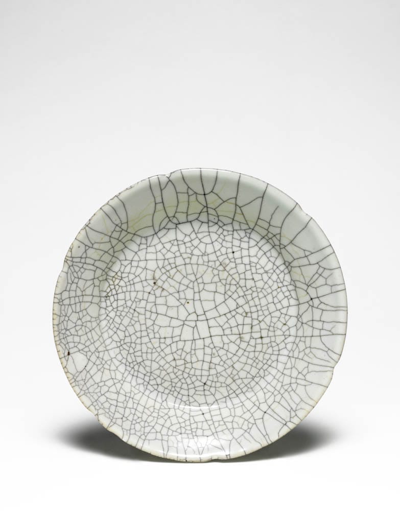 C.6-1968. Description Stoneware dish, with a thick, very pale greyish green opaque glaze with a dark grey fine crackle. Kuan type. The dish has a wide base and straight slanting sides. Six depressions in lip to represent flower petals. Convex central surface. The body is exposed at one place on the lip, and burnt reddish brown Short, glazed, tapering foot with unglazed rim burnt dark reddish brown. Glazed base. Bequeathed by Mrs Walter Sedgwick, 1968, through the National Art Collections Fund. From the Fitwilliam Collection