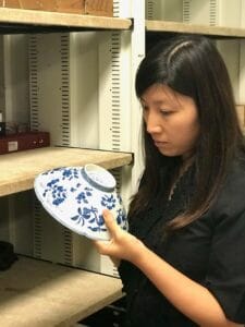 Vivian Tong inspecting a white and blue ceramic bowl.